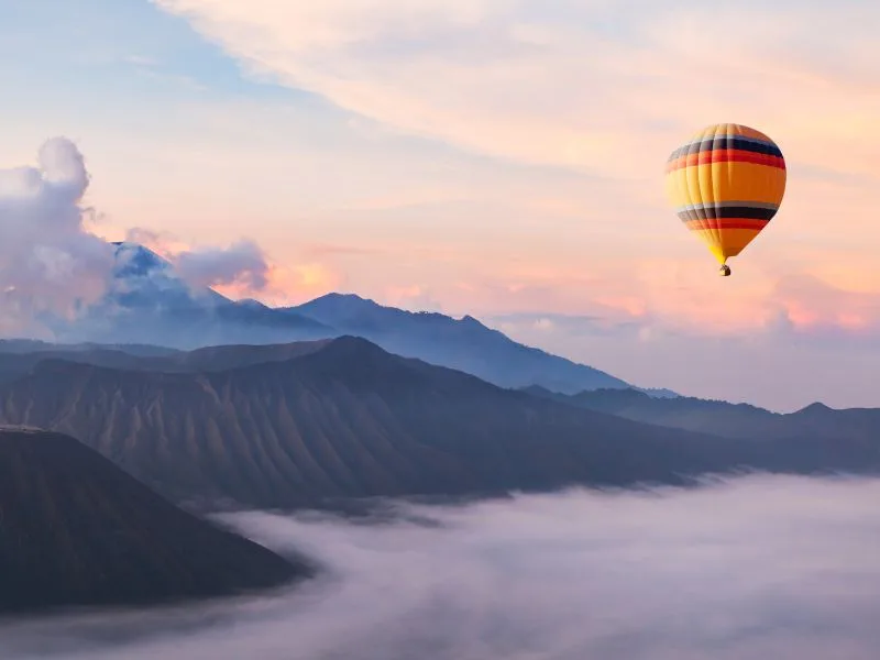 Hot air balloon over island cliffs at dawn with soft clouds